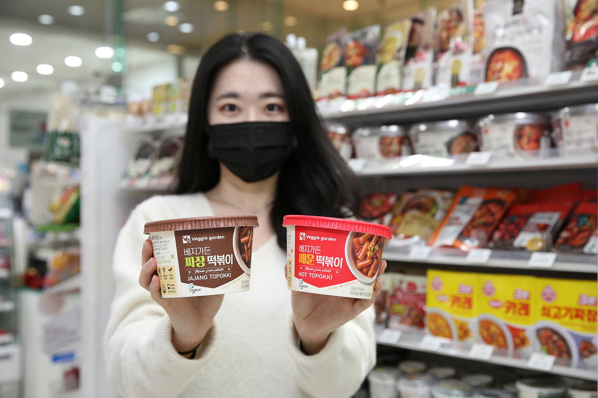 GS25 매장의 간편식 매대 앞에서 모델이 비건간편식 짜장떡볶이와 매운떡볶이를 들고 있다 (2)